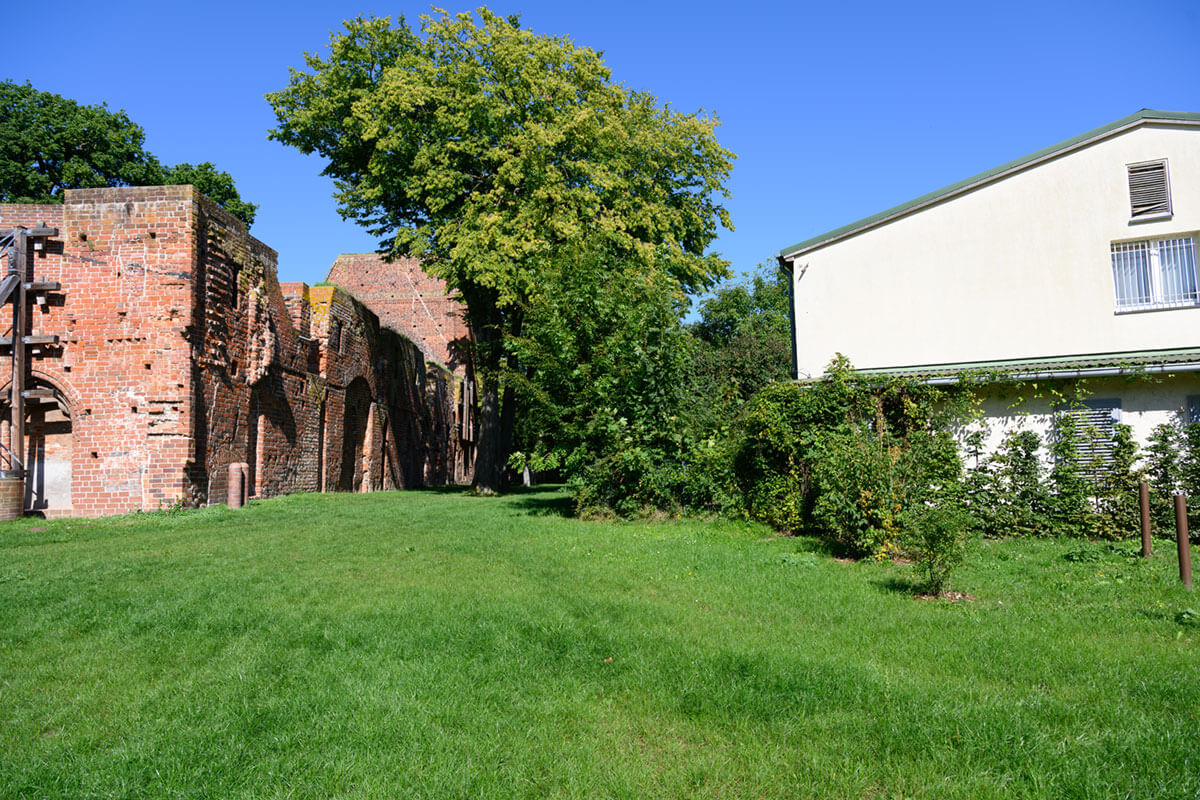Grünfläche mit historischen Backsteinmauern und modernem Gebäude, möglicher Einsatzort für Arbeitsgelegenheiten im Außenbereich.