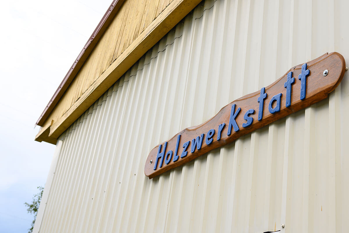 Außenansicht einer Werkstatt mit dem Schild „Holzwerkstatt“, Einsatzort für Maßnahmen zur Resozialisierung Straffälliger.